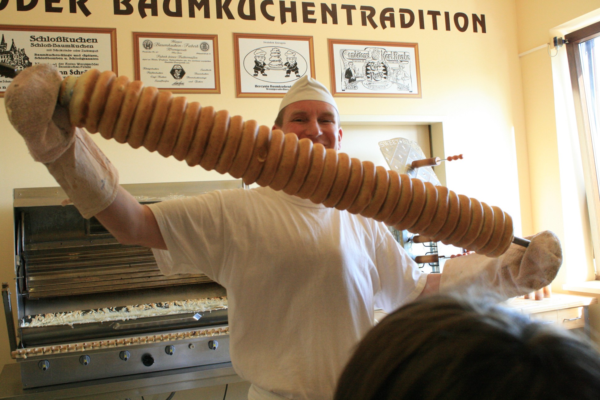 der Bäcker hält eine Walze mit Baumkuchen in den Händen